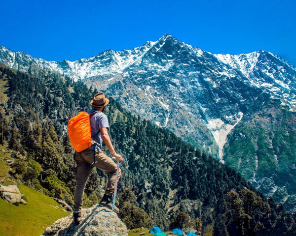 Man exploring breathtaking mountain scenery with snow-capped peaks under a clear blue sky.